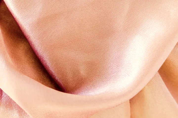 Tecido rosa claro com dobras suaves, textura delicada.