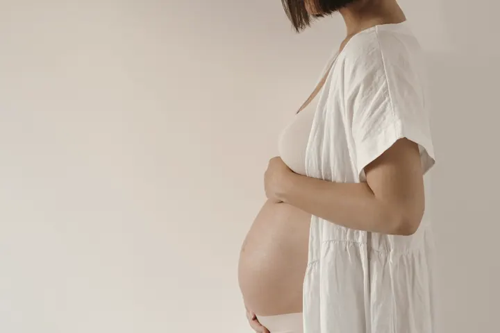 Gestante de branco tocando a barriga, retrato minimalista.